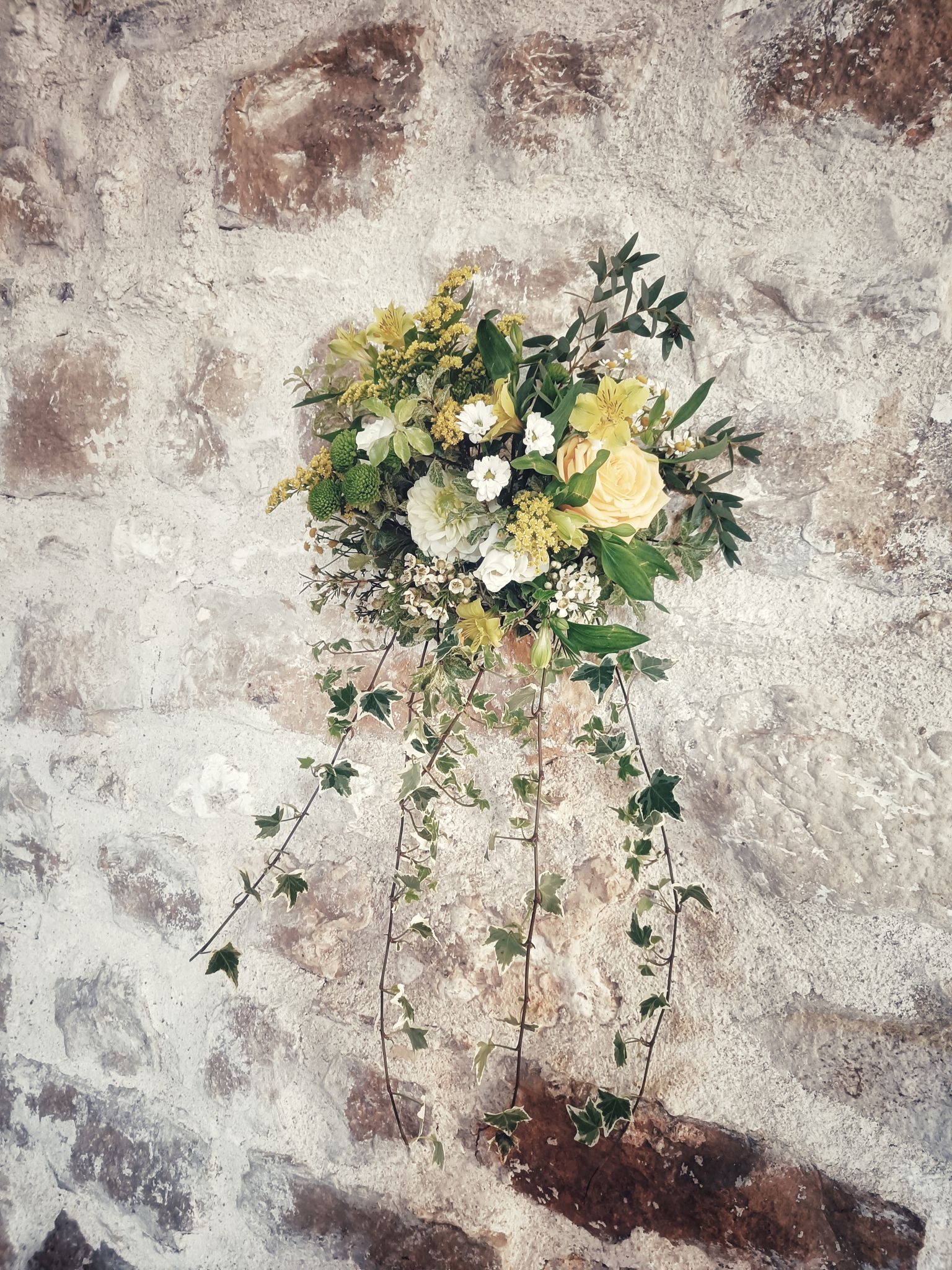 Mariage jaune blanc composition florale mur pierre